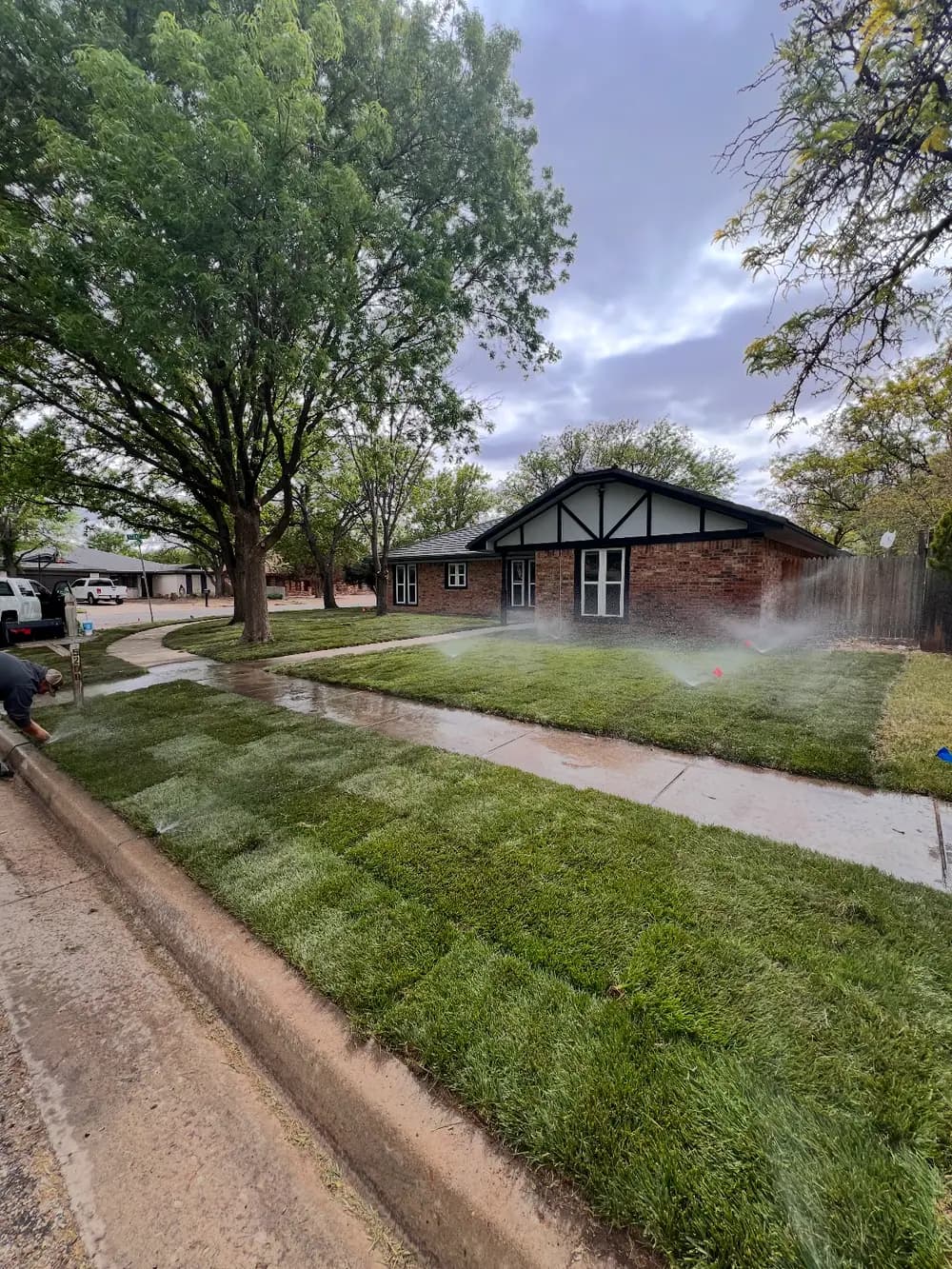Fresh sod and running sprinklers in front of a brick house